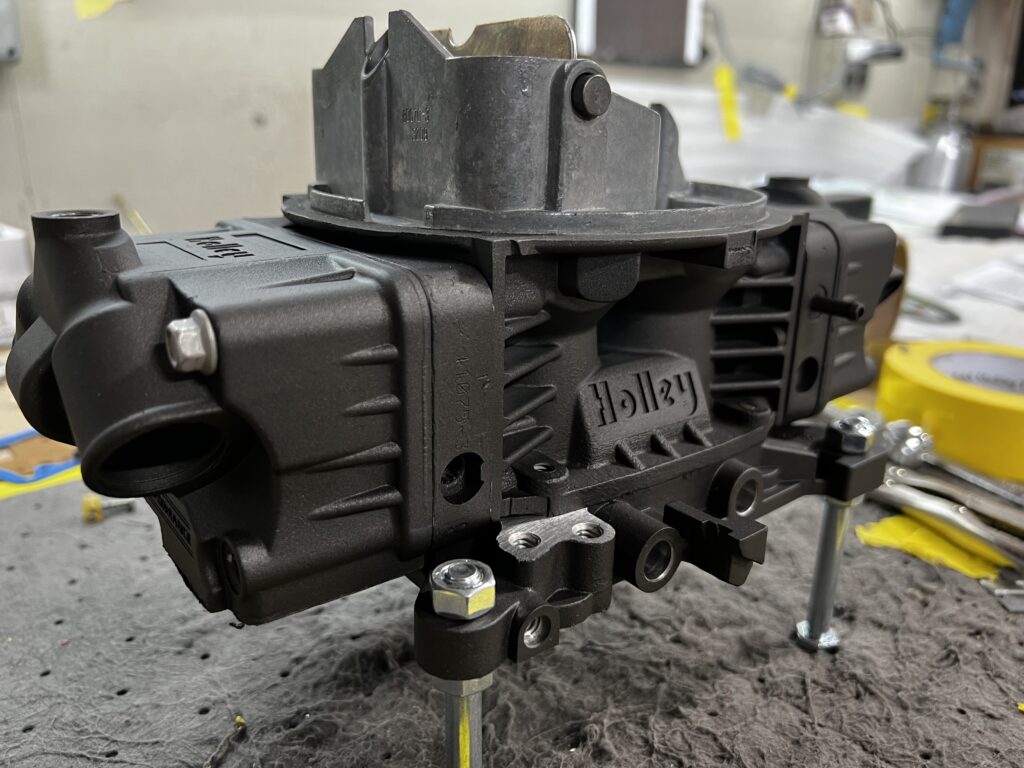 Black-coated Holley automotive component on a workbench at Carolina Finishing