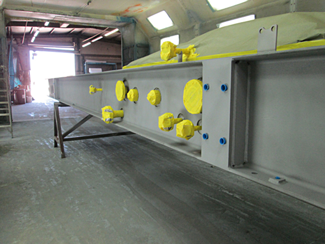 Fabricated metal beam with holes and mating surfaces protected by masking tape and plugs